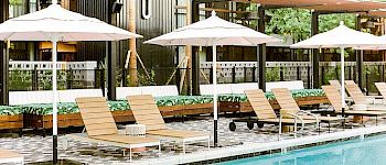 A resort pool area with sun loungers, white umbrellas, shaded seating, and wooden decking beside a clear blue pool, hotel-like and relaxing.