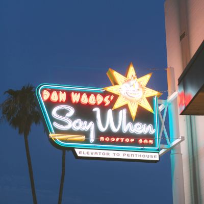 The image shows a neon sign lit up at dusk for "Say When Rooftop Bar" with palm trees silhouetted in the background.