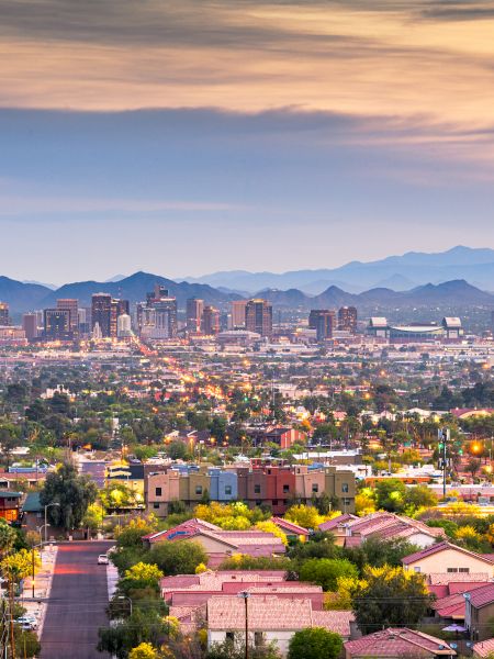 A cityscape with a mountainous backdrop at dusk, featuring a dense urban area transitioning into residential neighborhoods surrounded by greenery.