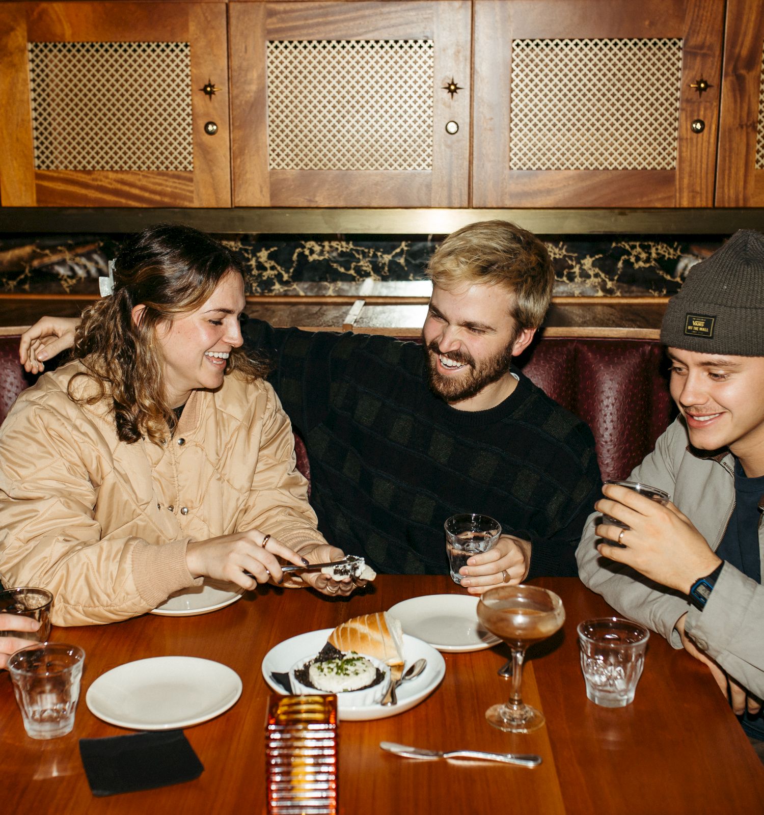 Five people are sitting at a table, sharing drinks and desserts, laughing and enjoying each other's company.