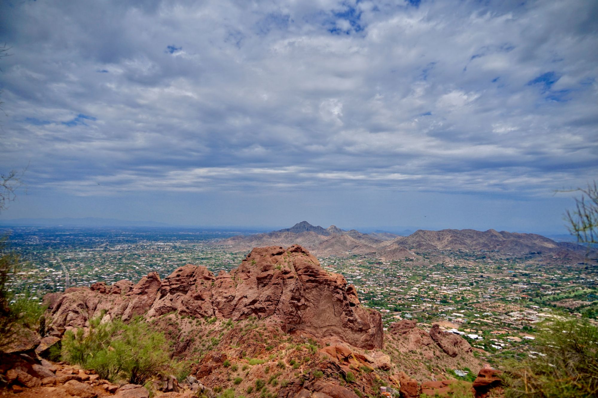 A scenic view of a rocky desert landscape with distant mountains under a partly cloudy sky, overlooking a sprawling city below.