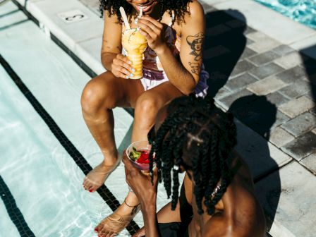 Two people are sitting by the poolside, enjoying drinks. They appear relaxed and are interacting with each other.