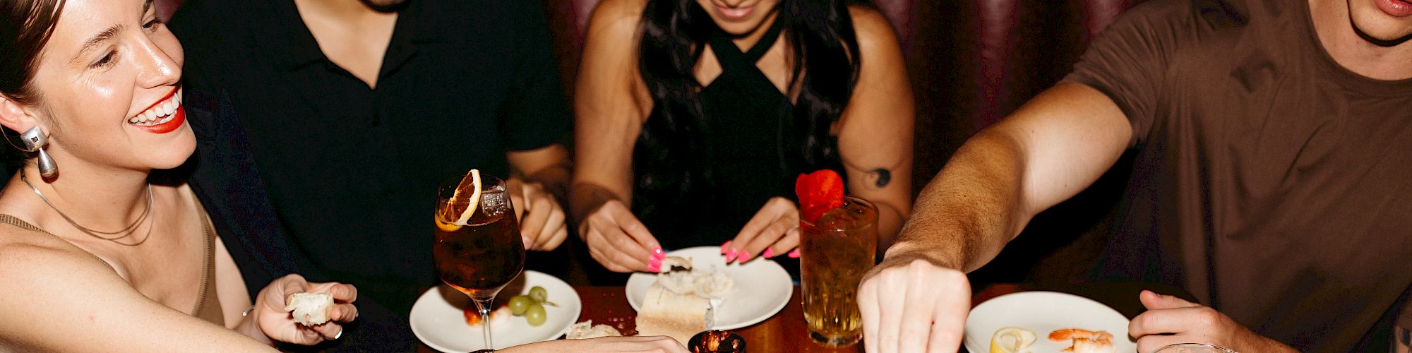 A group of people enjoying a meal at a restaurant with various plates of food and drinks on the table, sharing and laughing together.