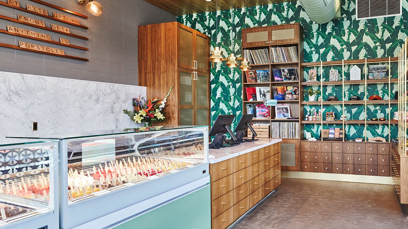 This image shows a brightly lit ice cream shop with colorful decor, gelato display cases, a wooden counter, and shelves with various items.