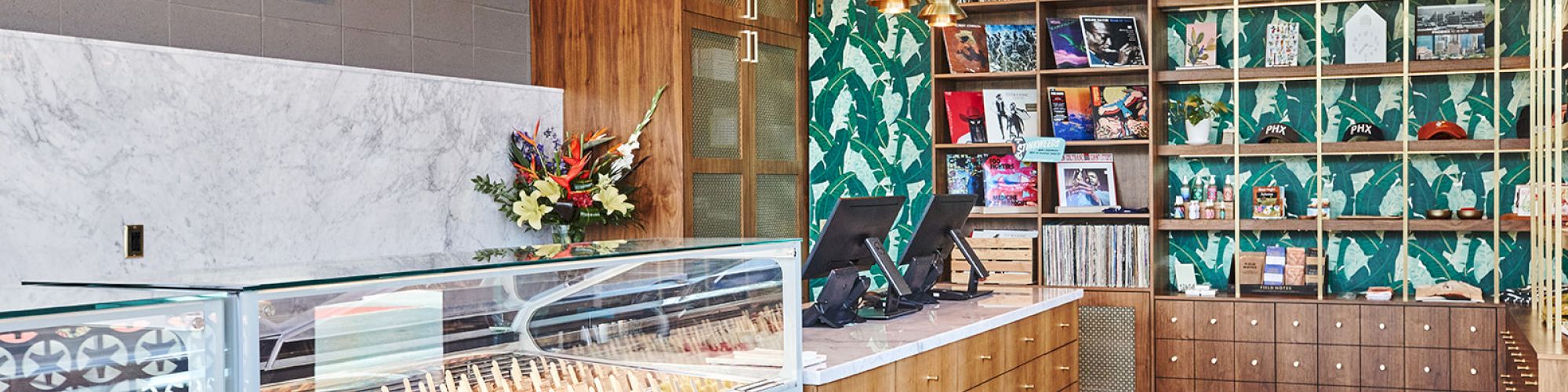 This image shows a brightly lit ice cream shop with colorful decor, gelato display cases, a wooden counter, and shelves with various items.