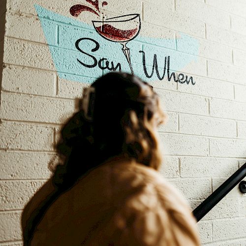 A person facing a brick wall with a drawing of a splashing cocktail and the words 