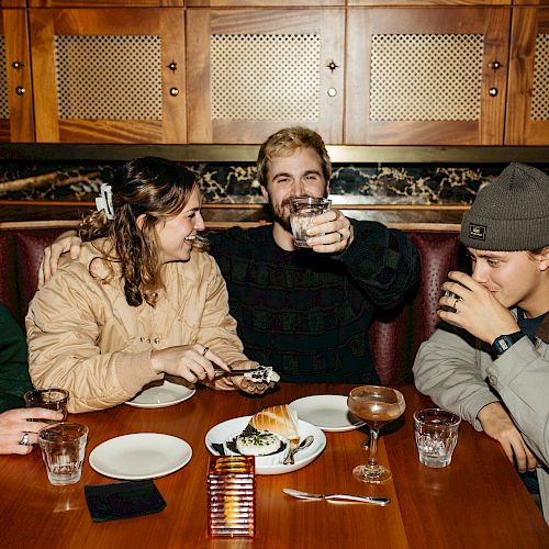 Five people sitting around a table, enjoying drinks and conversation in a cozy restaurant setting, with some food and drink on the table.