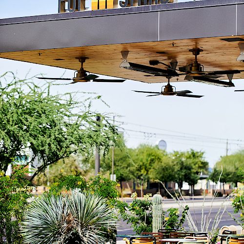 The image shows an outdoor seating area at a place called "Pop Stand," with greenery and several chairs and tables under a structure with fans.