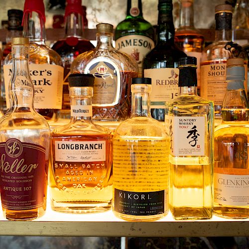 The image shows a variety of liquor bottles, including whiskey and other spirits, organized on a shelf.