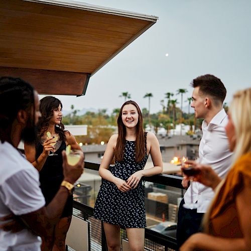 A group of people socializing on a rooftop, with some holding drinks, as they enjoy an evening gathering.