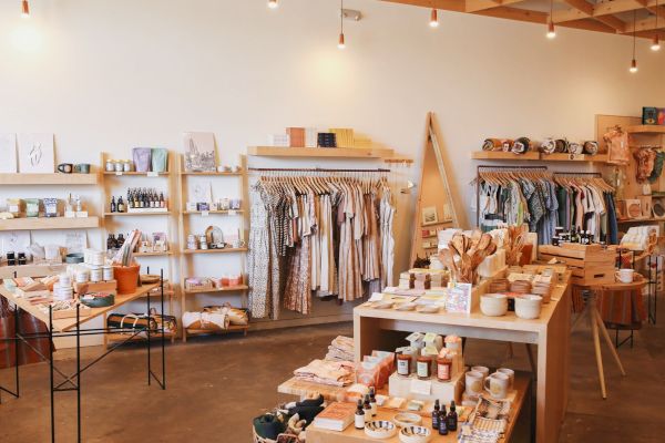 A beautifully arranged boutique store featuring clothing, skincare products, pottery, decor items, and various accessories displayed on shelves and tables.