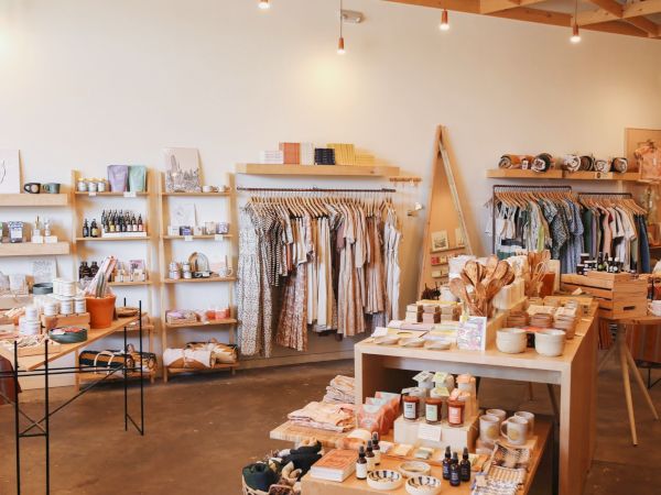 A beautifully arranged boutique store featuring clothing, skincare products, pottery, decor items, and various accessories displayed on shelves and tables.