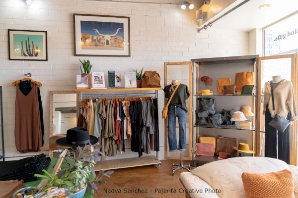 The image shows a boutique with clothing racks, mannequins, hats, and accessories. There's also wall art and potted plants for decor, ending the sentence.