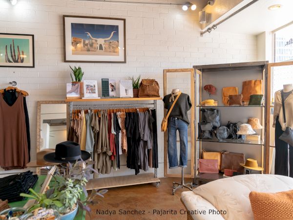 The image shows a boutique with clothing racks, mannequins, hats, and accessories. There's also wall art and potted plants for decor, ending the sentence.