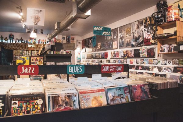 The image shows the interior of a record store with various vinyl records organized by genre, including Jazz, Blues, and Soul.