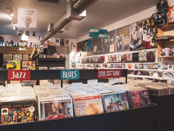 The image shows the interior of a record store with various vinyl records organized by genre, including Jazz, Blues, and Soul.