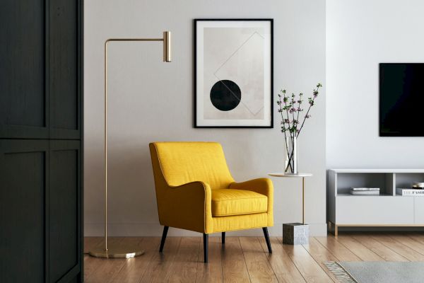 A modern living room with a yellow armchair, a floor lamp, wall art, a small table with flowers, and a TV on a white media console.