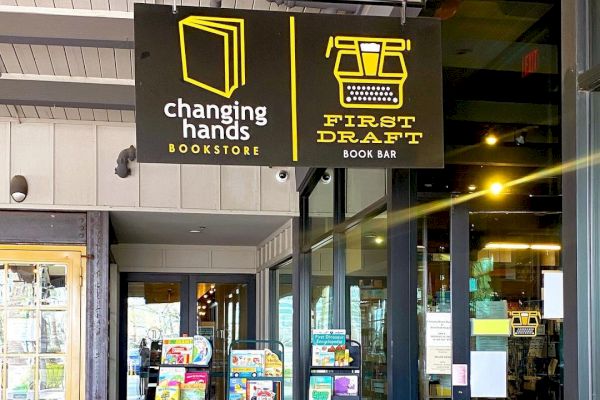 This image shows the entrance of Changing Hands Bookstore with shelves of books displayed outside and a sign for the First Draft Book Bar.