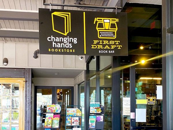 This image shows the entrance of Changing Hands Bookstore with shelves of books displayed outside and a sign for the First Draft Book Bar.