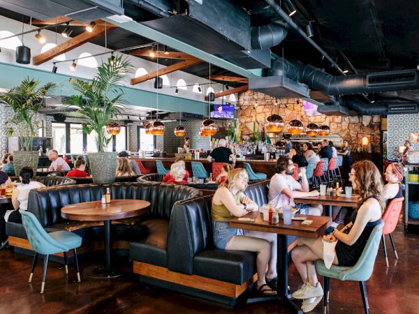 A bustling restaurant with patrons seated at tables and booths, enjoying meals under stylish lighting and decor.
