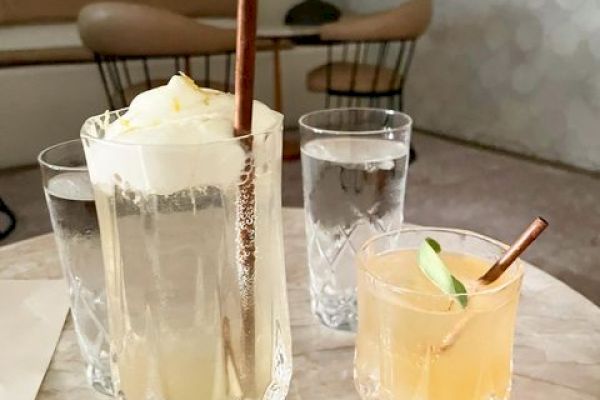 The image shows a table with two drinks; one with a straw and ice cream in a tall glass, and another with a lime slice and straw. Two glasses of water.