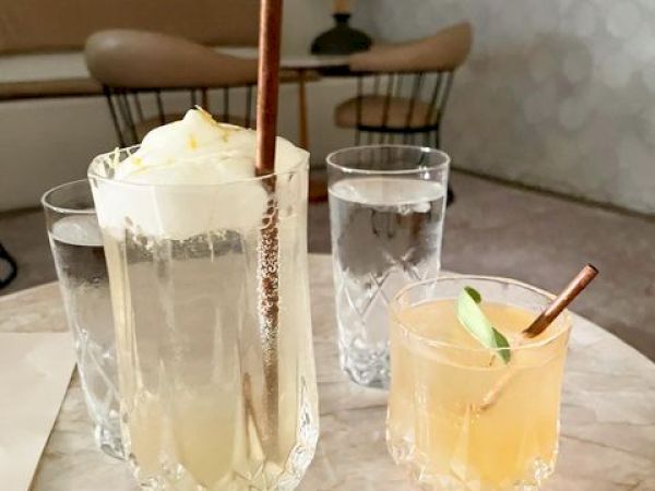 The image shows a table with two drinks; one with a straw and ice cream in a tall glass, and another with a lime slice and straw. Two glasses of water.