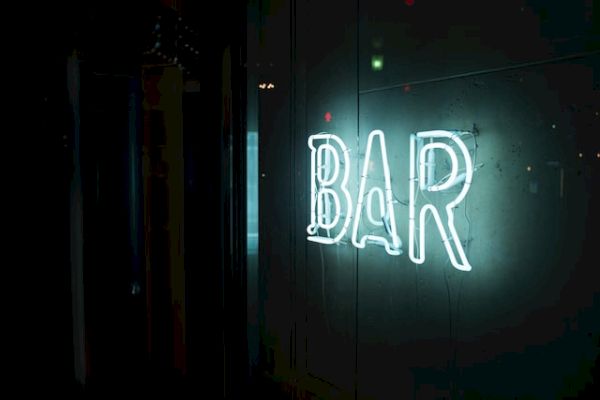 A glowing, neon "BAR" sign is illuminated against a dark background, giving a vibrant and inviting feel to the location.