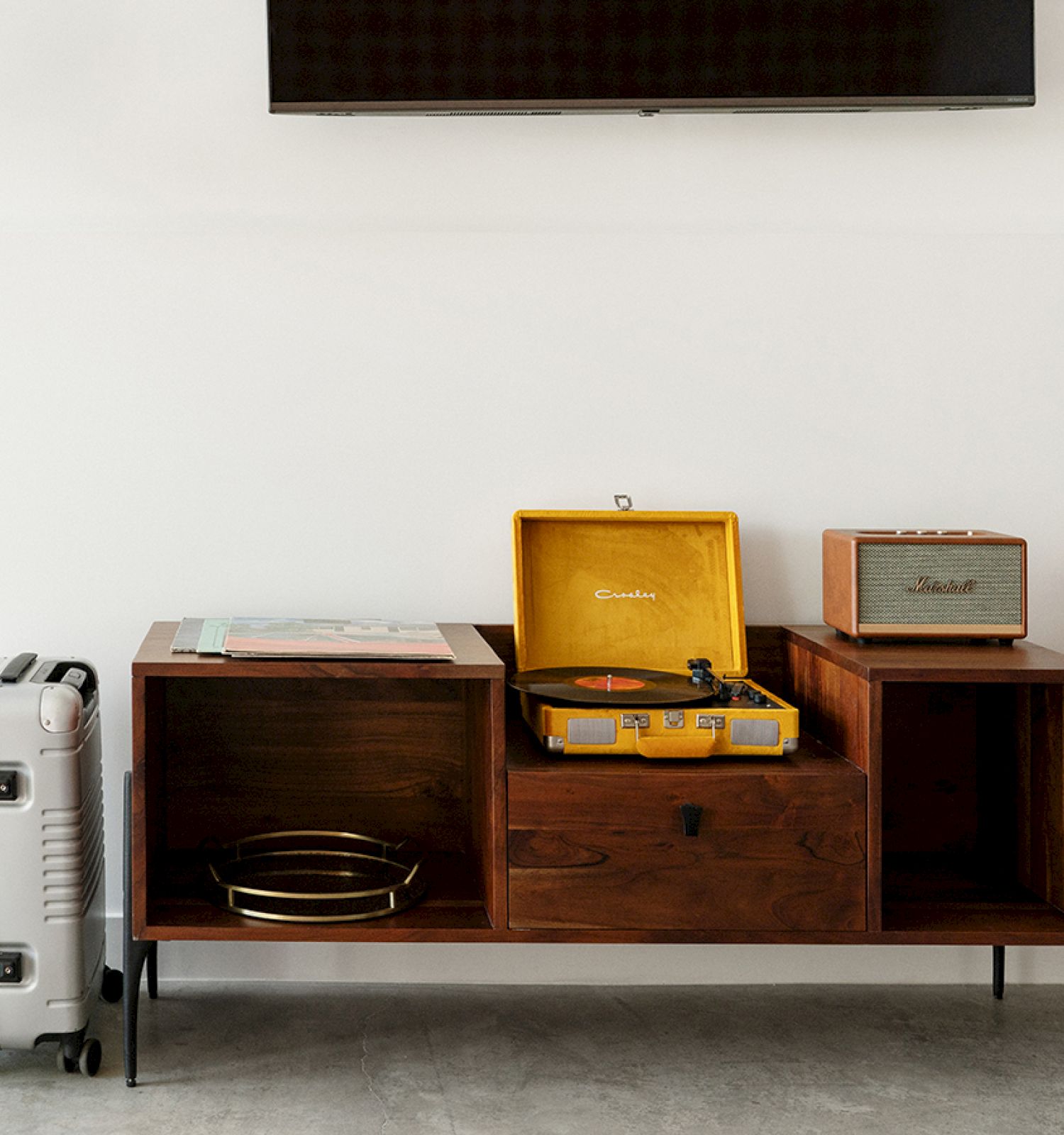 The image shows a modern room with a mid-century style wooden console, a record player, a suitcase, a speaker, and some decor items.