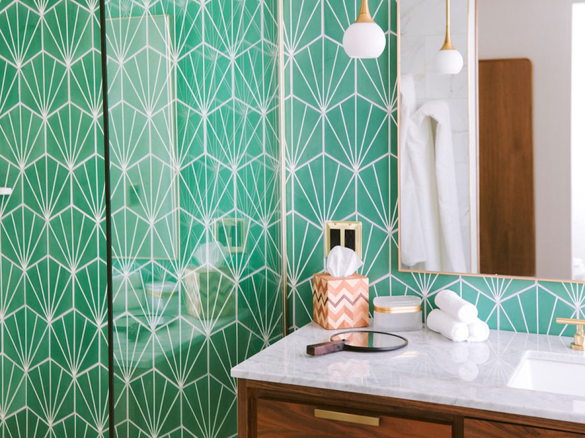 This image shows a modern bathroom with green geometric wallpaper, a wooden vanity with a white countertop, and a mirror above the sink.