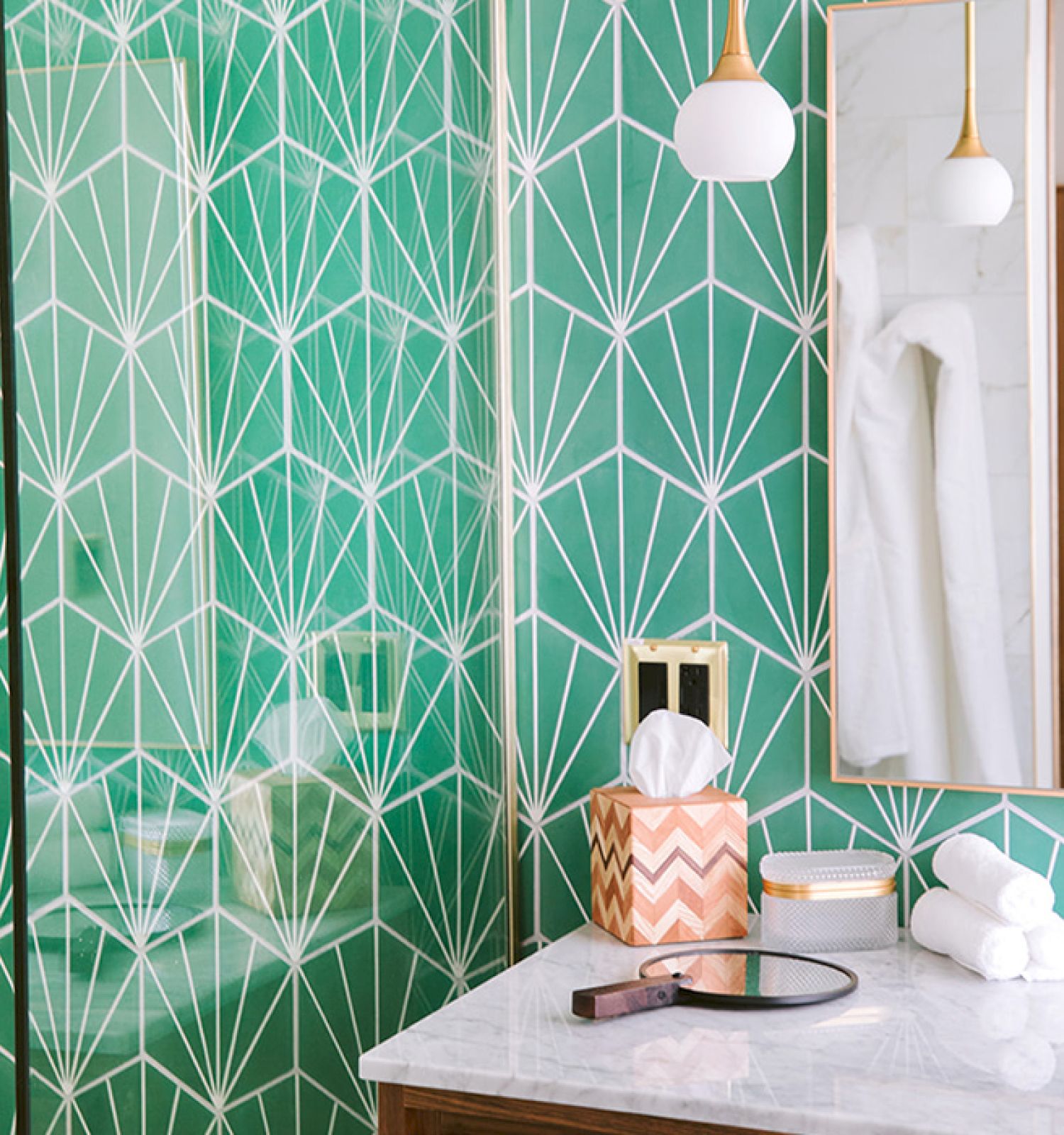 A bathroom with green and white geometric-patterned wallpaper, a mirror, a countertop with a tissue box, and rolled towels.