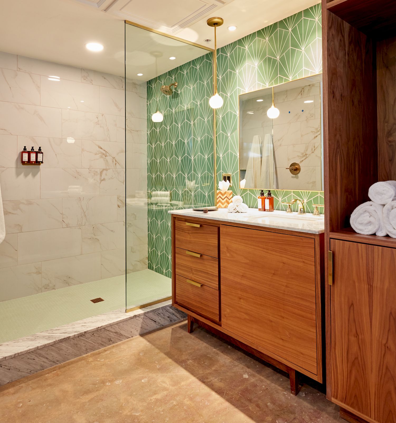 The image shows a modern bathroom with a glass shower enclosure, green-tiled accent wall, wooden vanity with sink, and a wooden closet with towels.