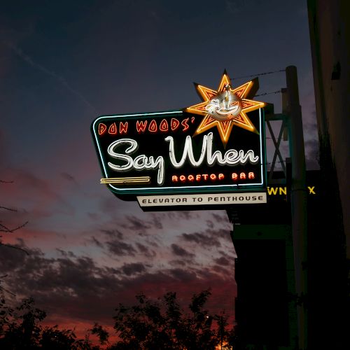 A neon sign for "Don Woods' Say When Rooftop Bar" with a sunset backdrop, directing to an elevator to the penthouse.