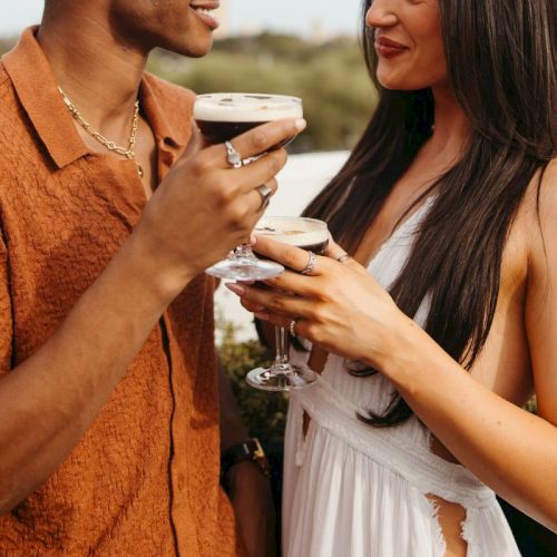 Two people holding espresso martinis, smiling at each other on a rooftop setting.