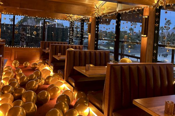 A restaurant with brown booths, gold balloons on the floor, and star-shaped lights hanging, creating a festive atmosphere.