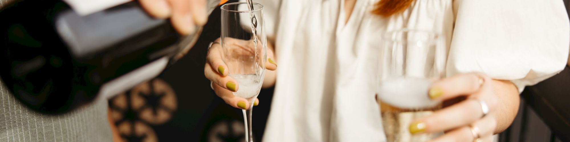 Two people enjoying a celebration, one pouring champagne into flutes, with a festive atmosphere in the background.