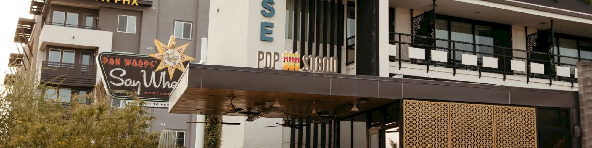 Modern building with signage for "Uptown PHX" and "Rise," surrounded by greenery and outdoor seating.