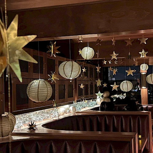 Decorated bar area with hanging star lanterns and paper lanterns, cozy booths, warm lighting, and mirrors reflecting the festive decor.