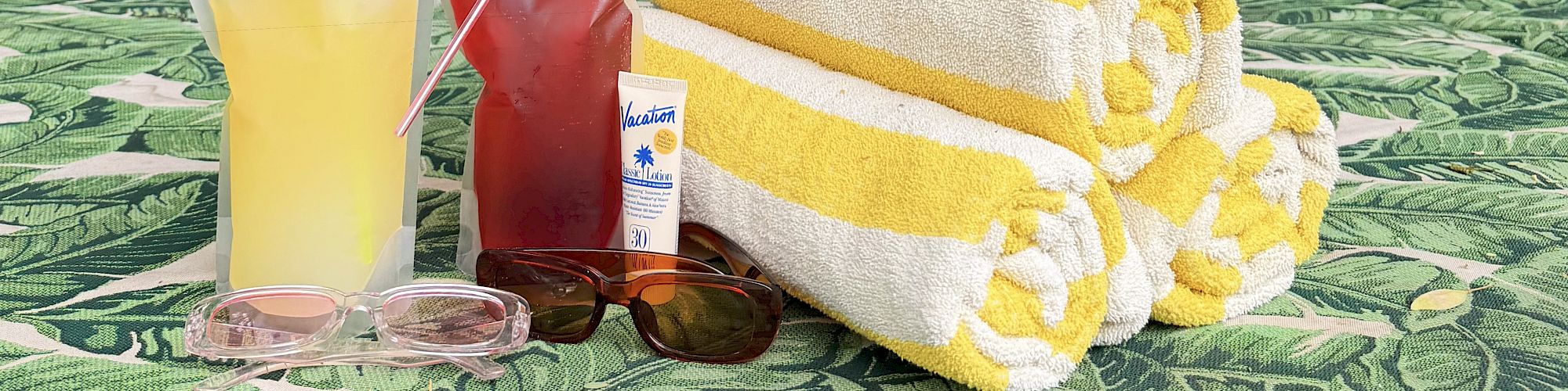 Two fruity drinks with colorful straws, sunny yellow towels, and sunglasses on a poolside table&mdash;summery refreshment vibes.