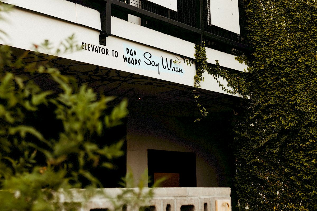 A building facade with lush greenery and a sign reading "Welcome to Say Ulita" above a rustic entryway.