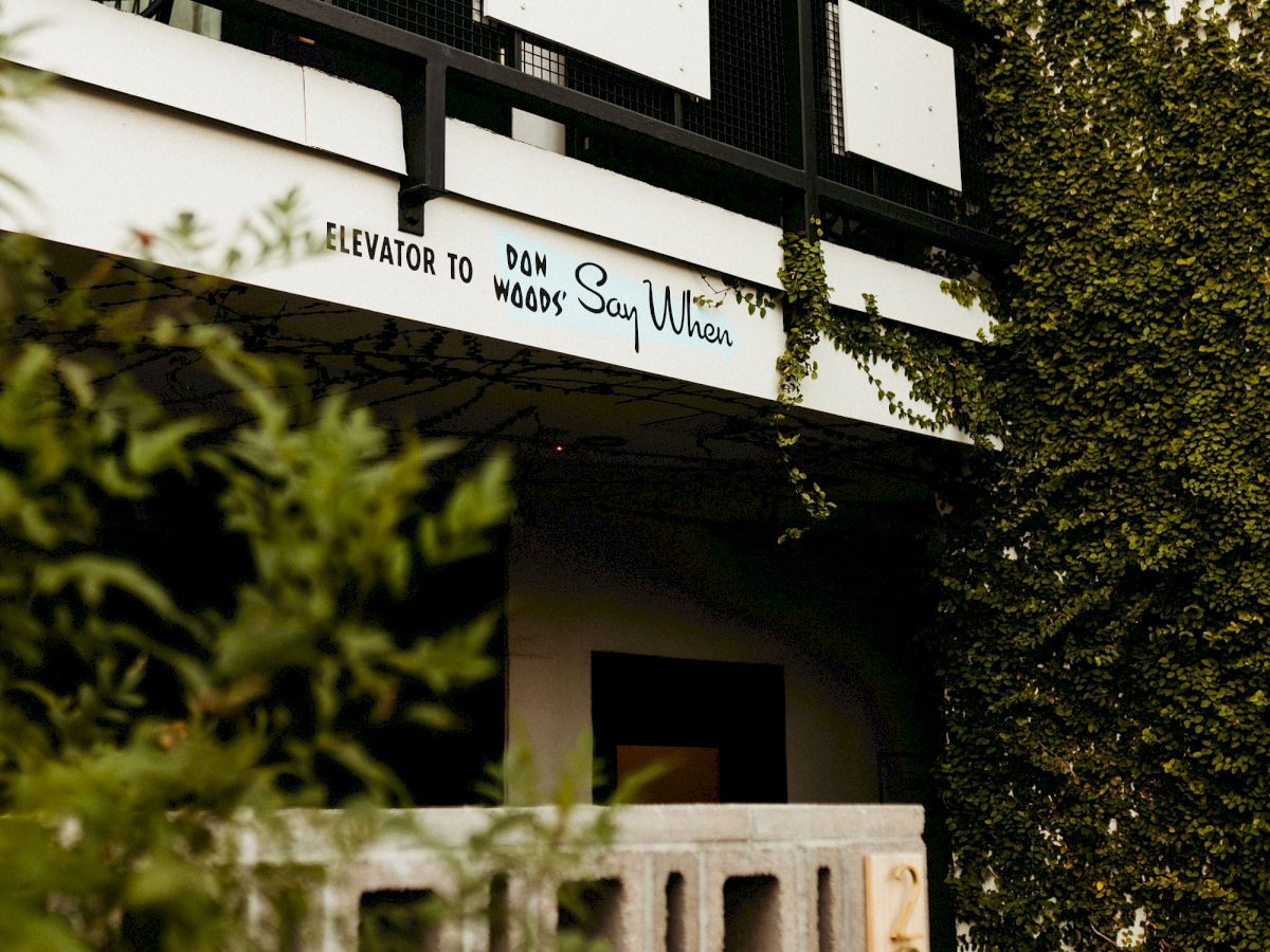 A building facade with lush greenery and a sign reading "Welcome to Say Ulita" above a rustic entryway.