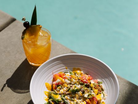 A tropical drink and a vibrant salad by a poolside, bathed in sunlight.