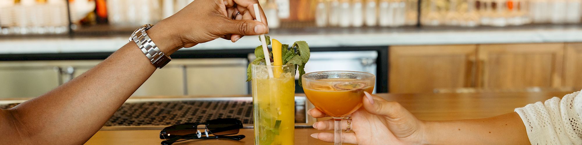 Two people clinking glasses with cocktails at a bar counter, creating a friendly and social atmosphere.