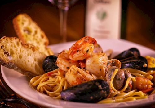 A plate of spaghetti with mussels and shrimp, topped with herbs, with garlic bread on the side.