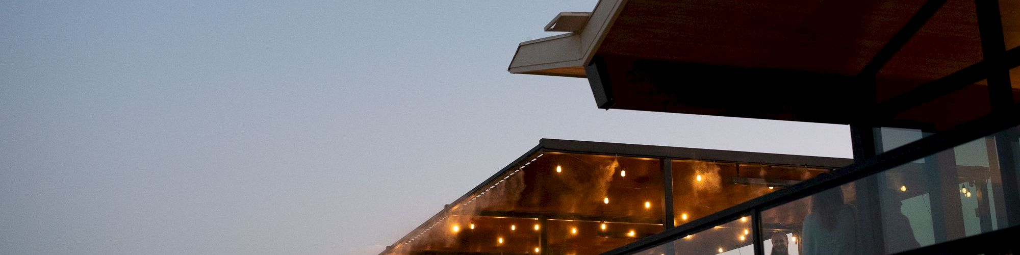A modern outdoor terrace with string lights and a red stairway under a twilight sky.