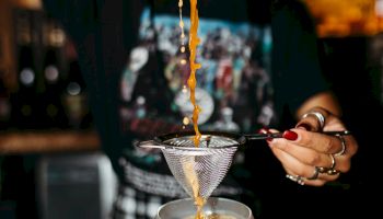 A person is pouring a drink through a strainer into a cocktail glass at a bar.