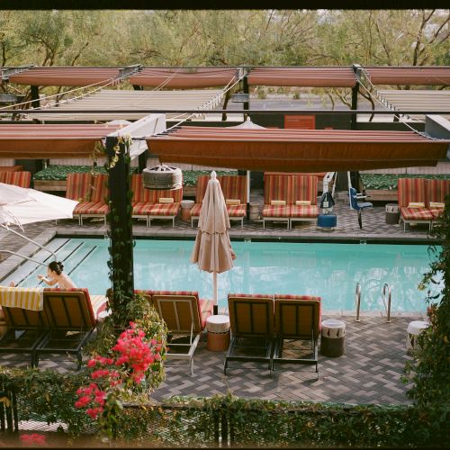 A tranquil poolside lounge area with sun loungers, umbrellas, and shaded cabanas, set among greenery and stone pavers.